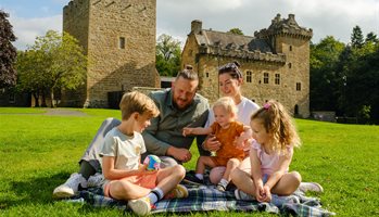 A family sitting on a picnic rug on the grass with the Dean Castle in the background